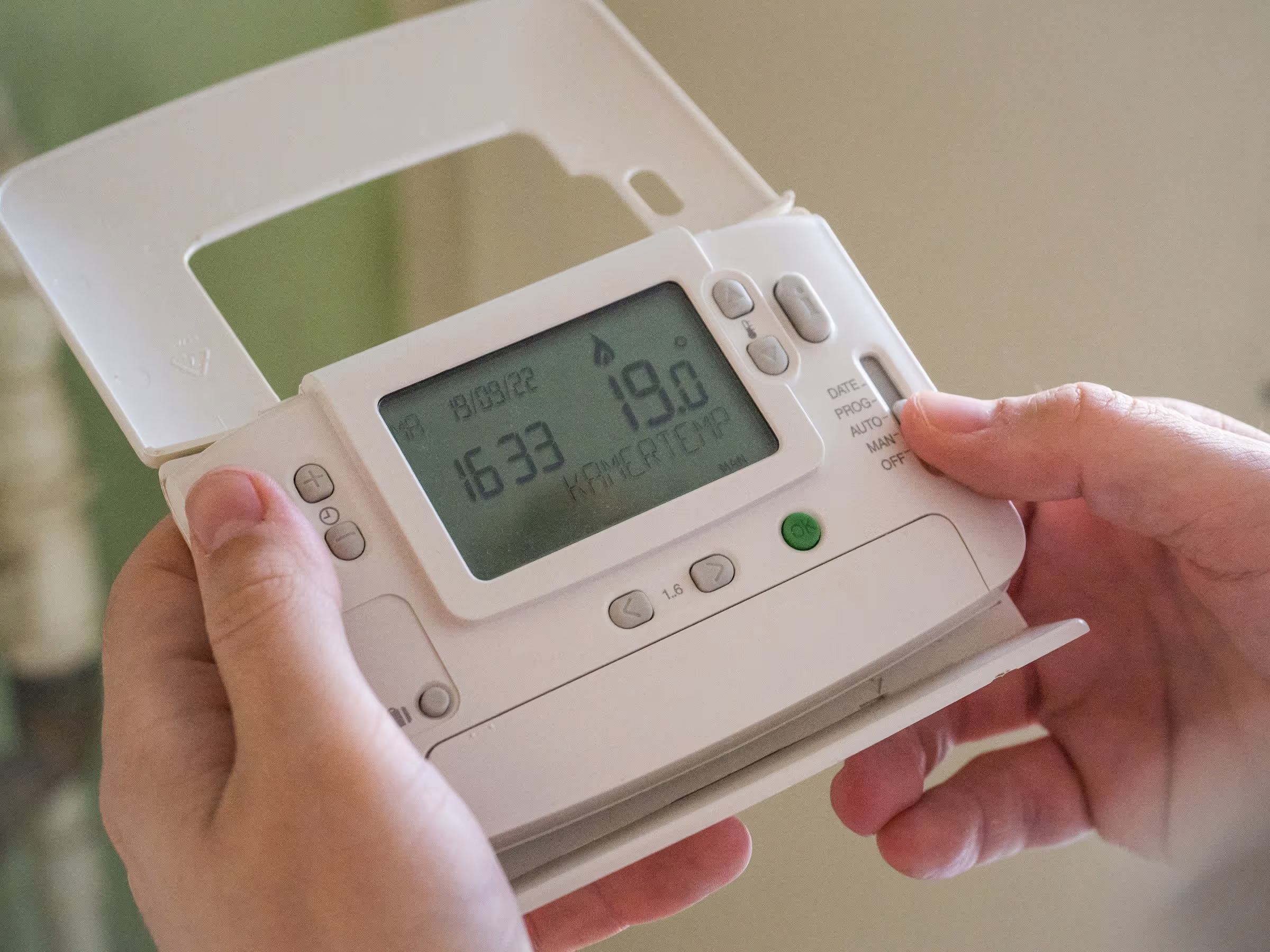 Eine Nahaufnahme einer Hand, die einen modernen digitalen Heizungsregler mit einem eleganten Touchscreen-Interface und Temperaturanzeige einstellt."