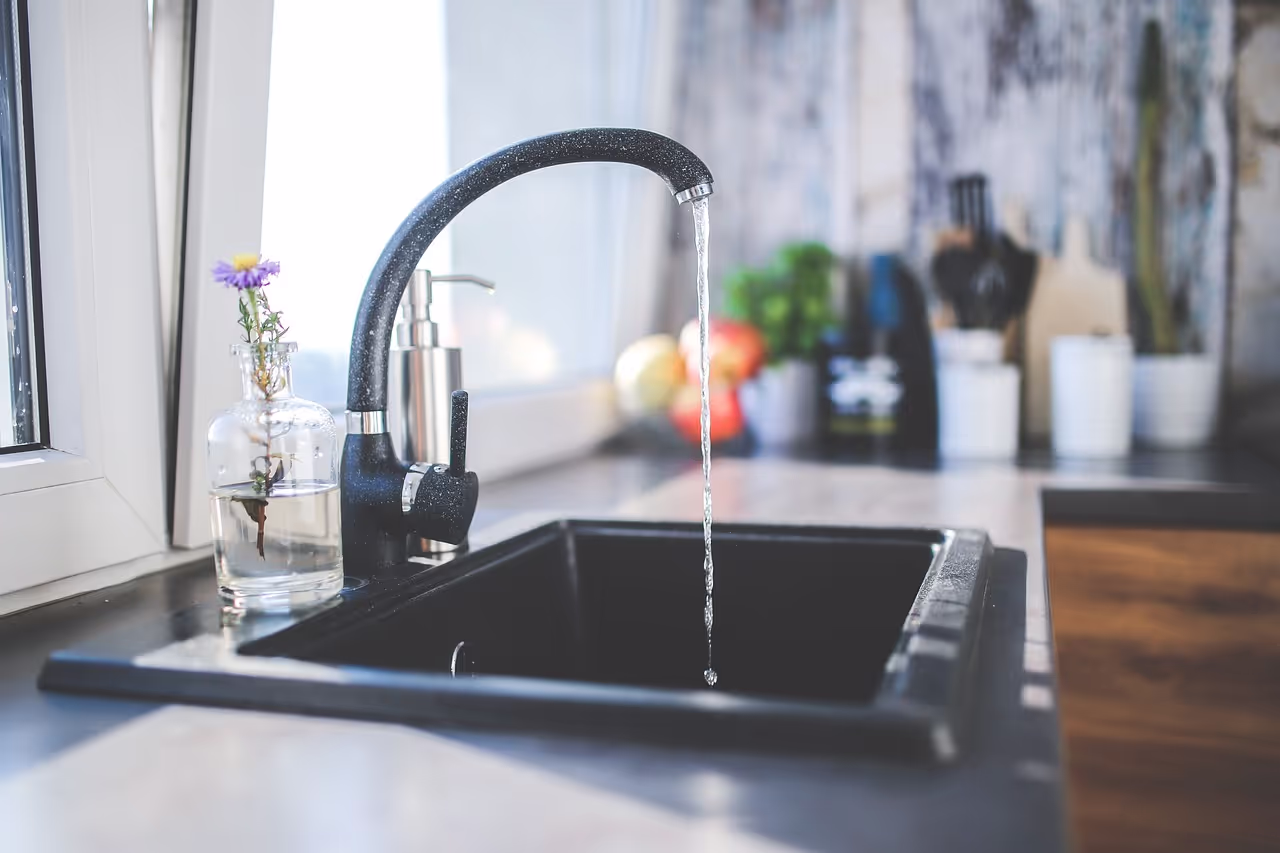 Detailaufnahme eines Wasserhahns mit fließendem Wasser in einer modernen Küche.